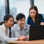 Fresh graduate sedang berdiskusi di kantor sambil melihat laptop untuk mencari peluang loker entry level dan memulai karier pertama