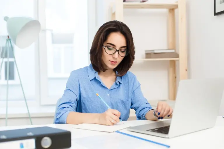 ilustrasi fresh graduate perempuan berbaju biru sedang mengerjakan dummy project untuk portofolio di depan laptop sambil menulis ide dan perencanaan proyek.