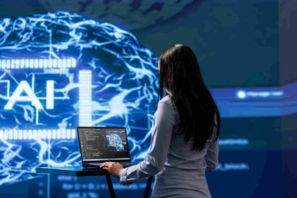 Ilustrasi seorang profesional menggunakan laptop di depan visualisasi otak digital AI yang menggambarkan perkembangan teknologi serta pentingnya skill yang tidak bisa digantikan AI seperti kreativitas dan berpikir kritis di dunia kerja.