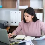 Seorang wanita muda berbaju pink yang sedang membuat dummy project data entry untuk pemula