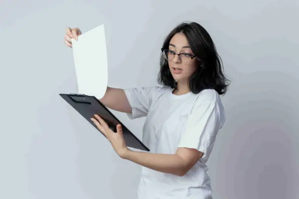 Seorang mahasiswa berkacamata dan berbaju putih sedang melihat contoh proposal magang mandiri untuk dijadikan referensi.