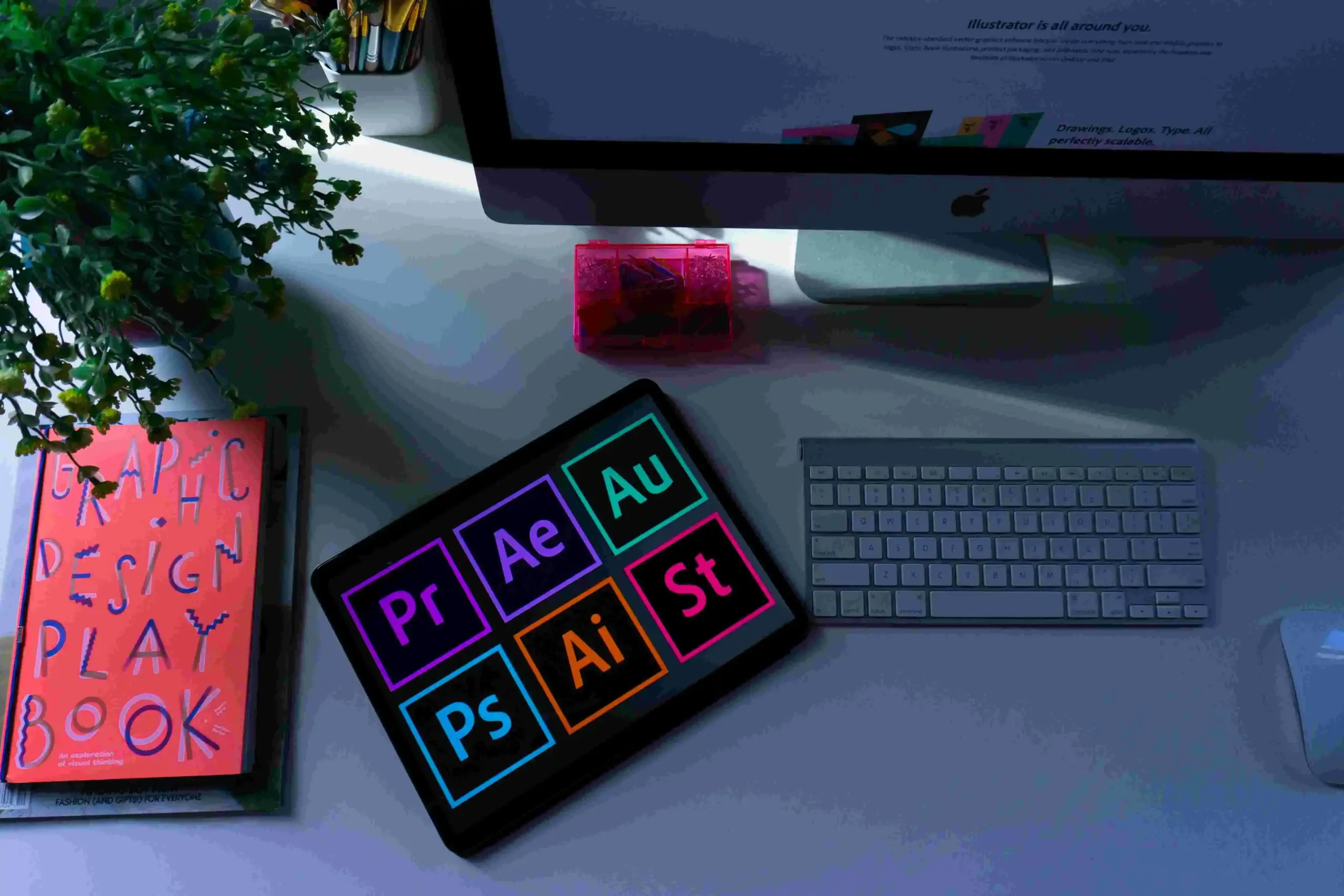 Setup desainer grafis dengan tablet menampilkan ikon Adobe Premiere, After Effects, Photoshop, dan Illustrator di atas meja studio kreatif.