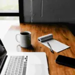 Setup kerja profesional dengan laptop, catatan, dan kopi sebagai gambaran rutinitas belajar sertifikasi business development.